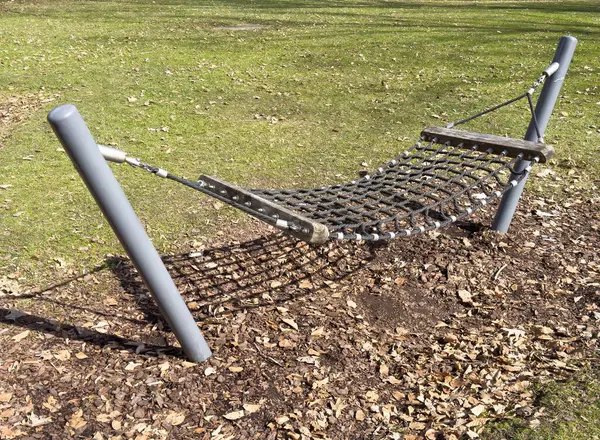 Dışarıdaki hamak yeşil çimlerde sallanıyor ve parkta metal direkler var..