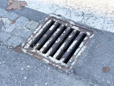 Düşen yapraklar ve çatlaklarla şehir asfalt sokağında paslı ızgara..