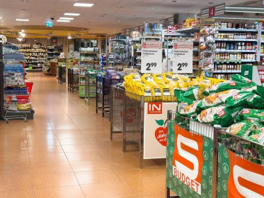 Market koridorunda alışveriş arabalarında sergilenen abur cuburlar ve ev eşyaları..