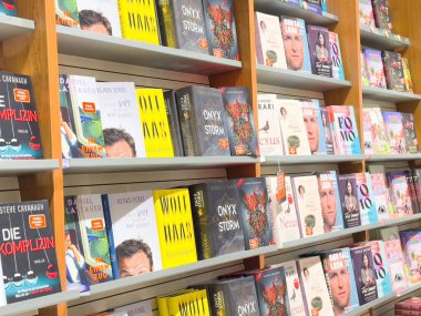 Bir mağazada çeşitli kitap kapakları bulunan kitaplık görüntüsü.