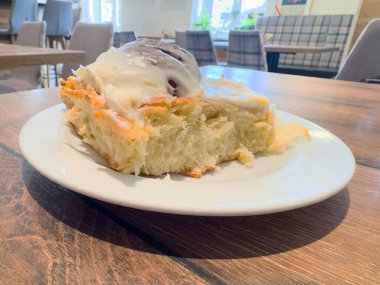 Taze tarçınlı rulo kremalı beyaz tabakta, rahat kafe ortamında..