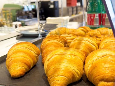 Fırın tezgahında altın kruvasanlar ve arka planda köpüklü su şişeleri..