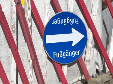 Şehir ortamında kırmızı çitli ve yön oklu ters yaya işareti.