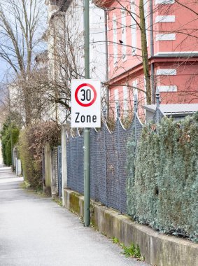 Banliyö sokağında zincir çitli ve ağaçlı hız sınırı 30 tabelası.