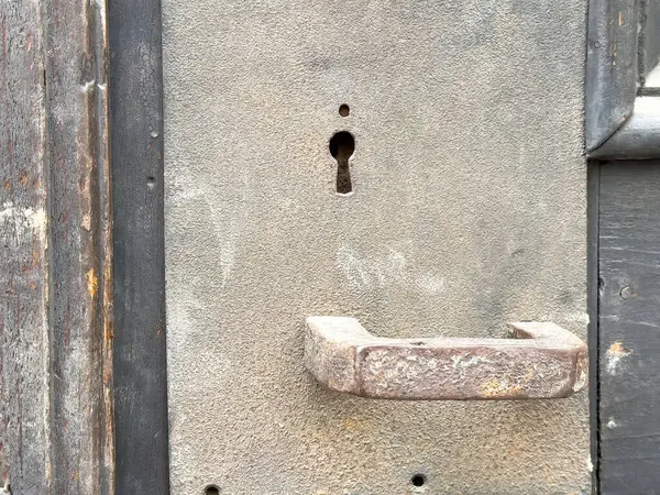 Anahtar deliği ve ahşap çerçevede yıpranmış sapı olan taşralı metal bir kapı..