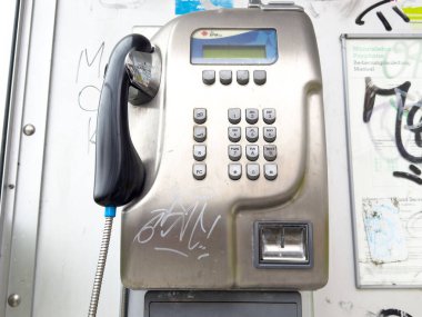 Grafiti etiketli ankesörlü telefon şehir ortamında dijital ekranlı.