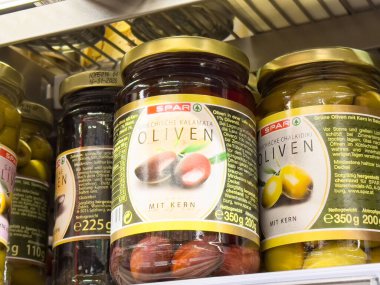 Süpermarket rafında Yunan ve tebeşir etiketli çeşitli zeytin kavanozları.