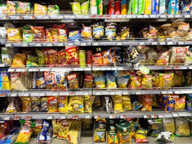Süpermarket raflarında çeşitli atıştırmalık paketler: cips, patlamış mısır ve krakerler.