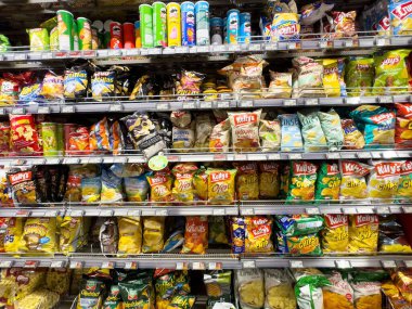 Süpermarket raflarında gösterilen paketlenmiş abur cubur çiplerinin çeşitliliği.