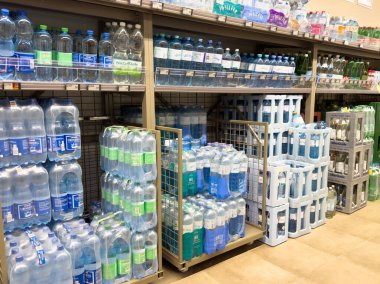 Süpermarket koridorunda çeşitli marka ve boyutlarda şişelenmiş su rafları.