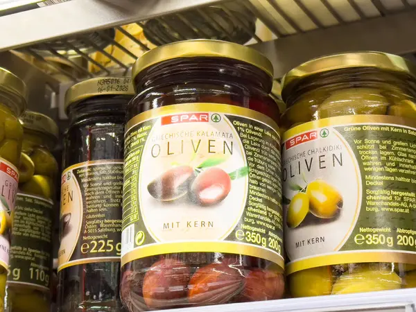 Süpermarket rafında Yunan ve tebeşir etiketli çeşitli zeytin kavanozları.