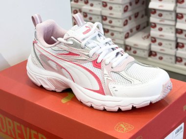 Arka planda üst üste dizilmiş ayakkabı kutularıyla birlikte beyaz ve pembe spor ayakkabıları sergileniyor..