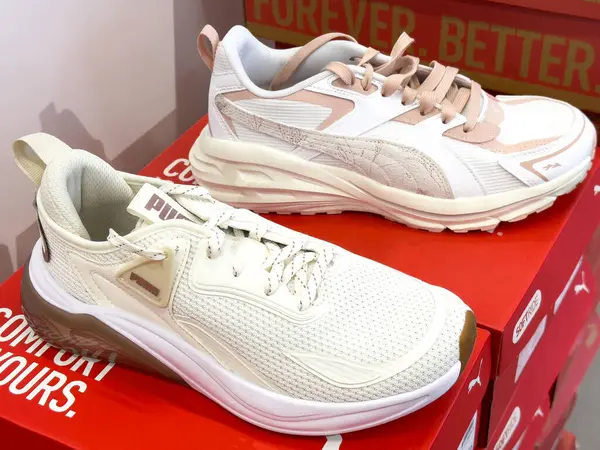Puma logolu kırmızı kutuların üzerinde beyaz ve bej spor ayakkabılar..