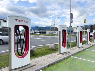 Tesla süperşarj istasyonu bulutlu bir günde yoğun yol ve dağların yanında.