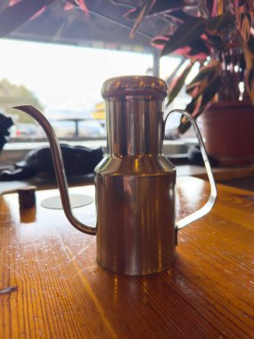Saf kafe ortamında ahşap masada paslanmaz çelik yağ sürahisi..