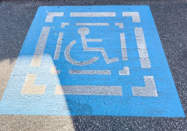 Asfalt üzerinde gölgeli mavi engelli parkı işareti.