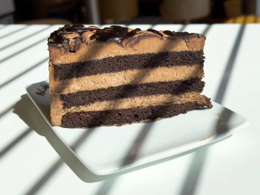 Güneş ışığında beyaz tabakta lezzetli çikolata katmanlı kek..