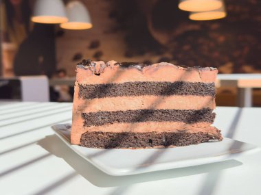 Güneşli kafede beyaz tabakta lezzetli bir dilim çikolatalı pasta..