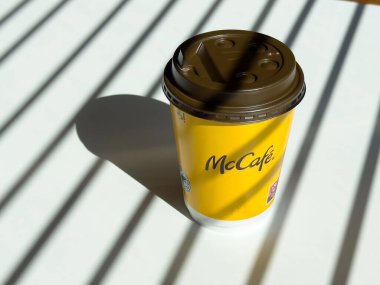 Mccafe kahve fincanı güneşli masada, gölgeli minimalist ortamda..