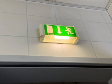 Fayanslı tavanda aydınlatılmış acil çıkış tabelası.