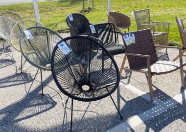 Açık hava pazarında güneşli havada gösterilen hasır ve metal sandalyeler.