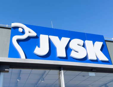 Açık mavi gökyüzüne karşı logosu olan Jysk mağaza önü.