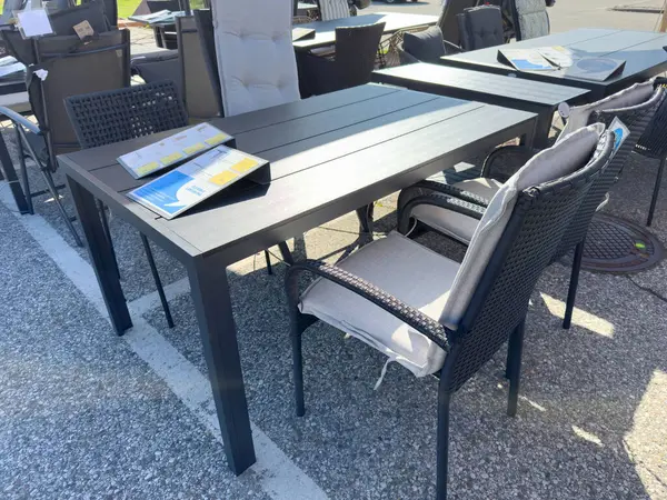 Açık teras mobilyaları, siyah masa ve kaldırımda sergilenen minderli sandalyeler..