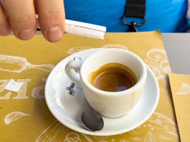 Kafe ortamında espresso 'ya şeker ekleyen bir erkek.
