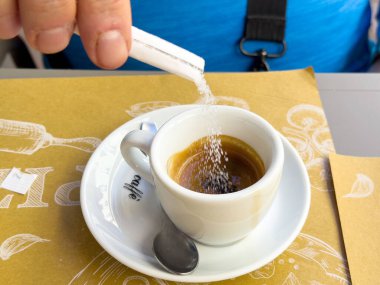 Kafe masasındaki espresso bardağına şeker döken bir erkek..