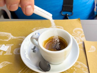Kafkasyalı erkek kahve masasındaki beyaz bardakta espressoya şeker ekliyor..