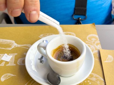 Kahverengi kağıt masadaki beyaz bardakta espressoya şeker ekliyorum..