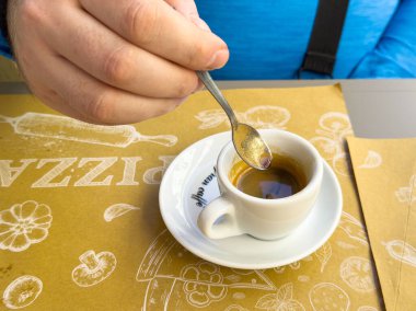 Erkek, kahve içmekten zevk alıyor. Kafe masasında küçük bardaklar karıştırıyor..