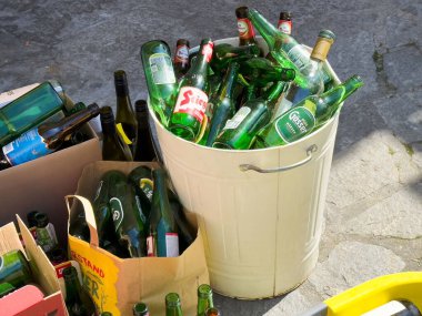 Boş yeşil bira şişeleri ve karton torbalarla doldurulmuş geri dönüşüm kutusu..