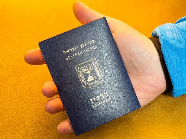Sarı yüzeyde, Kafkas erkek eli ile İsrail pasaportu yakın plan..