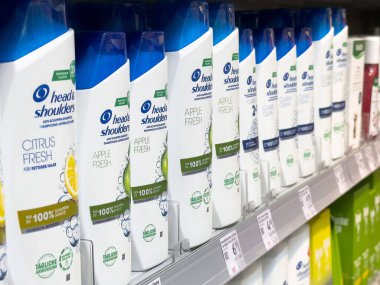 Kafası ve omuzları markalı raflarda çeşitli şampuan şişeleri var..