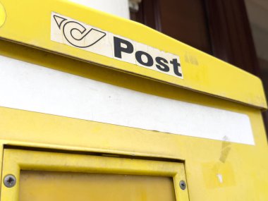 Şehir caddesinde logosu olan sarı posta kutusu.