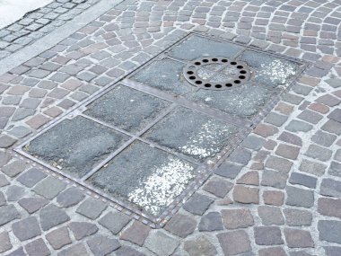 Çakıl taşı caddesinde dikdörtgen metal rögar kapağı..