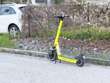 Yol kenarında sarı elektrikli scooter. Şehir merkezinde beyaz arabanın yanında..