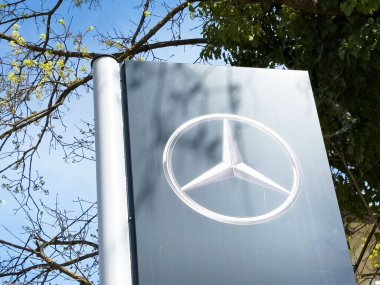 Arka planda ağaçlar olan açık hava tabelasına Mercedes-Benz logosu.