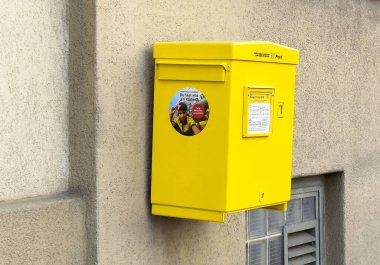 Kabataslak desenli duvara yapıştırılmış parlak sarı posta kutusu..