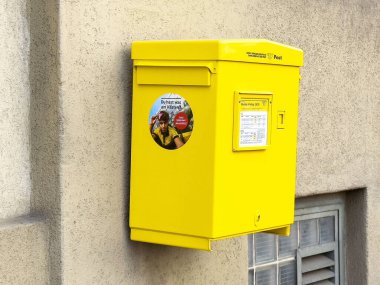 Uyarı ve bilgi paneli ile duvara iliştirilmiş parlak sarı posta kutusu.