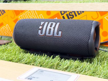 Yeşil çimlerin üzerinde turuncu markalı JBL bluetooth hoparlörü.