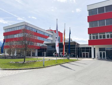 Önünde bayraklar ve güneşli bir günde kırmızı aksanlı modern ofis binası.
