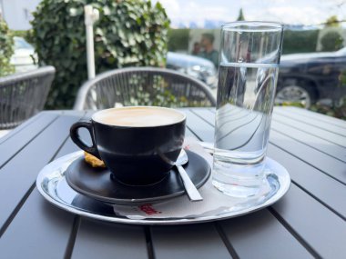 Güneşli ortamda kahve ve su bardağıyla açık kafe masası..