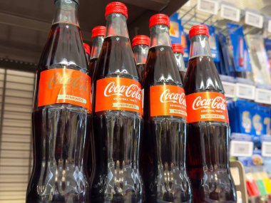 Mağaza rafında kırmızı etiketli klasik Coca-Cola şişeleri.