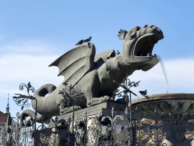 Şehir parkındaki mavi gökyüzü arka planı ve kuş detaylarıyla ejderha çeşmesi heykeli.