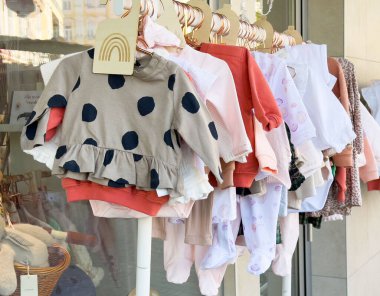Renkli bebek kıyafetleri vitrinde çeşitli şekillerde asılı duruyor..