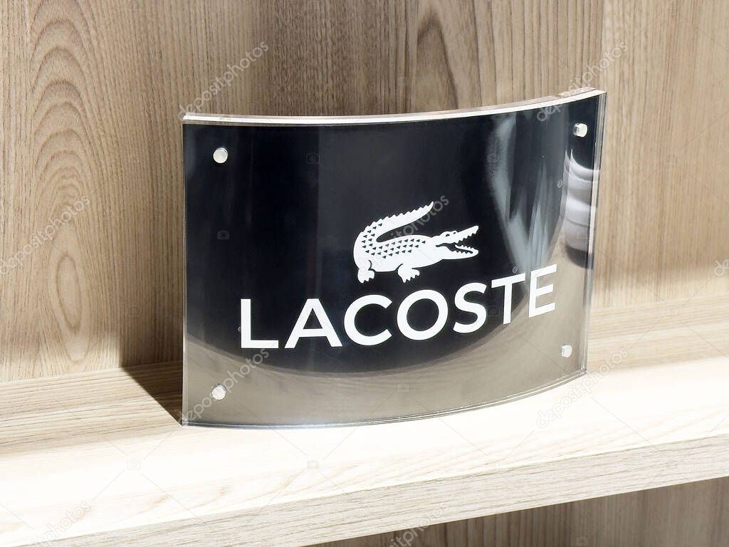 Lacoste logo sign on wooden shelf display with crocodile emblem.