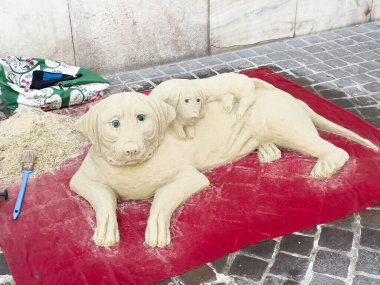 Labrador köpeği ve köpek yavrusunun kumdan heykeli kırmızı battaniyenin üzerinde..