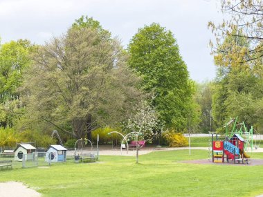 Villach, Avusturya - 17 Nisan 2025: Oyun yapıları ve köpek evleri ile renkli oyun alanı, ağaçlarla dolu yemyeşil bir alana kurulmuş, açık hava eğlencesine davet edilen